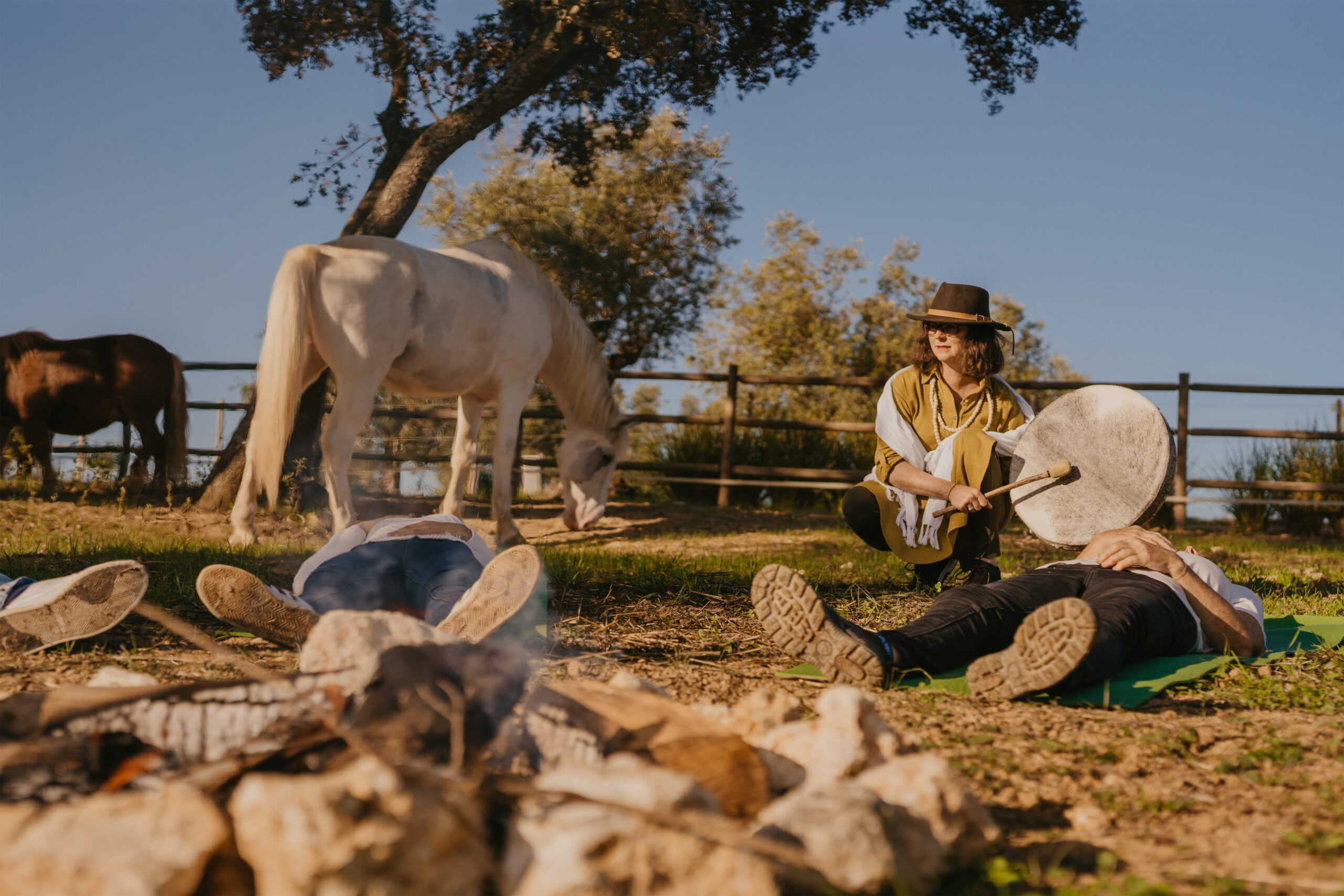 a lady playing a drum with the horses and group of people lying on the ground which looks like a ritual ceremony